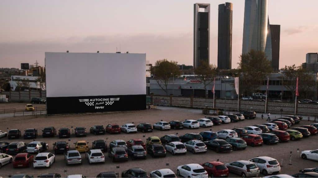 Pantalla de Autocine Madrid con coches aparcados y las Cuatro Torres al fondo