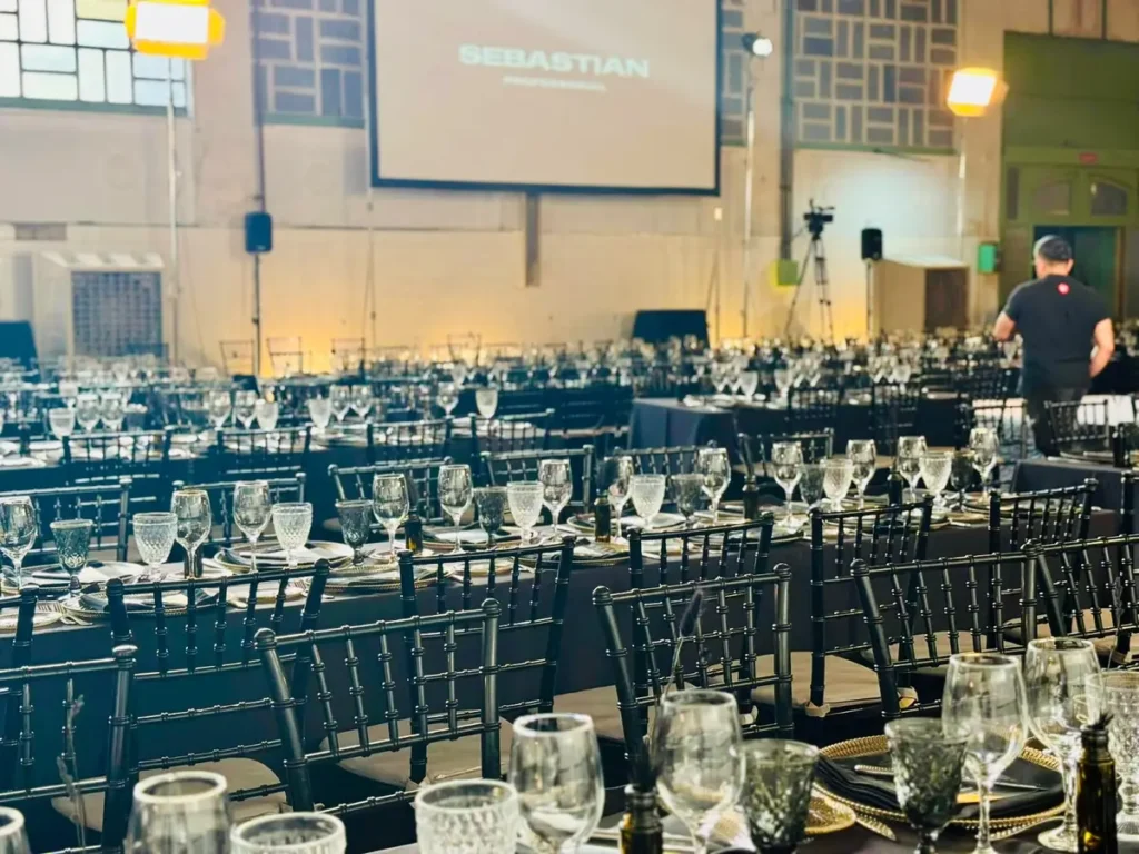 A ballroom at a major corporate event set up for a banquet, with tables draped in black tablecloths, black chairs, and glassware set out for hundreds of guests